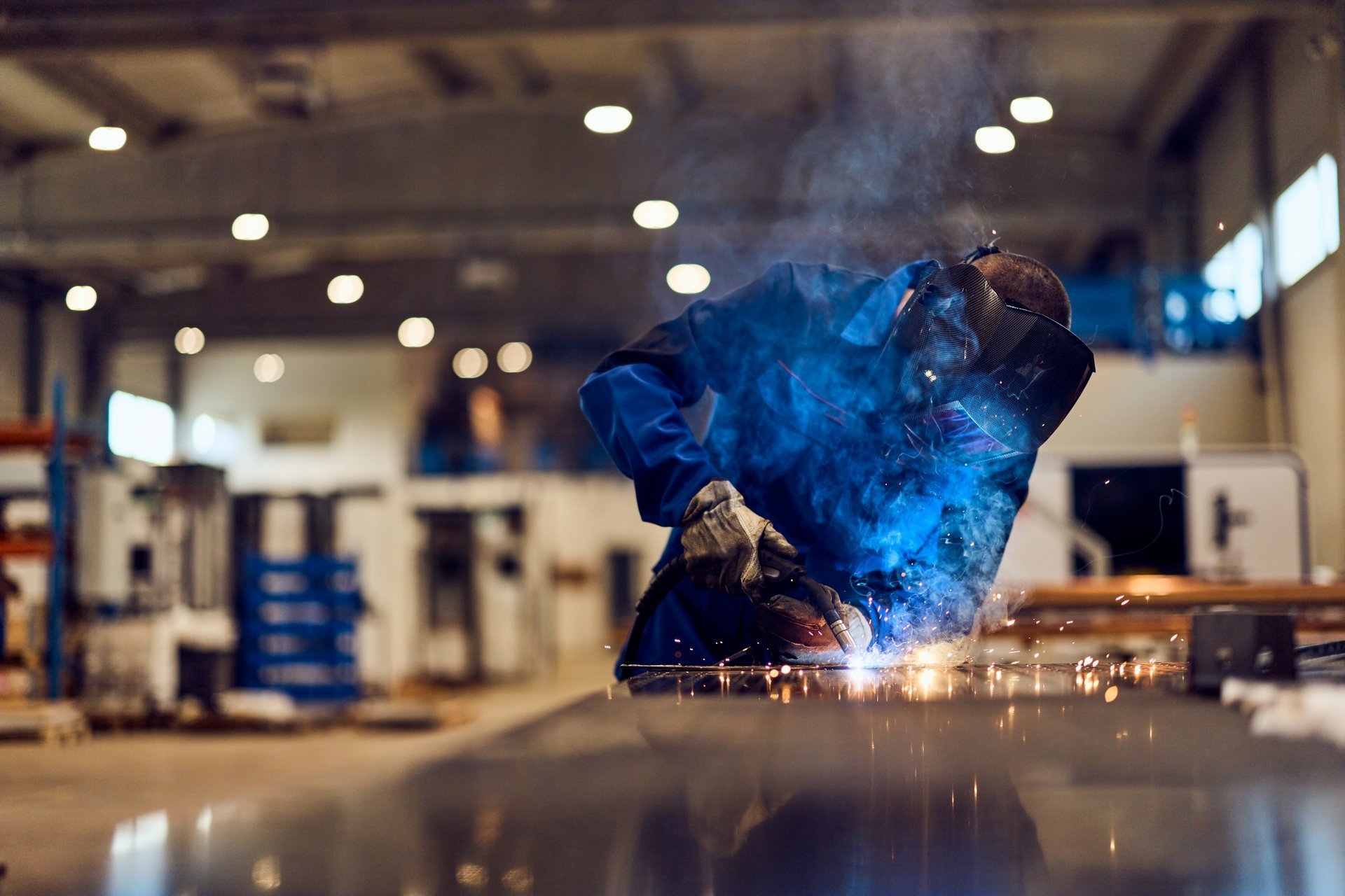Worker welding metal in a factory workshop with sparks