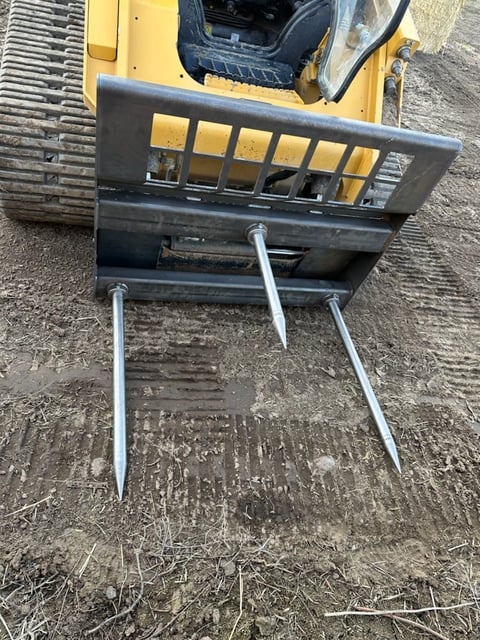 Overhead view of a black forklift attachment with metal tines mounted on a yellow vehicle