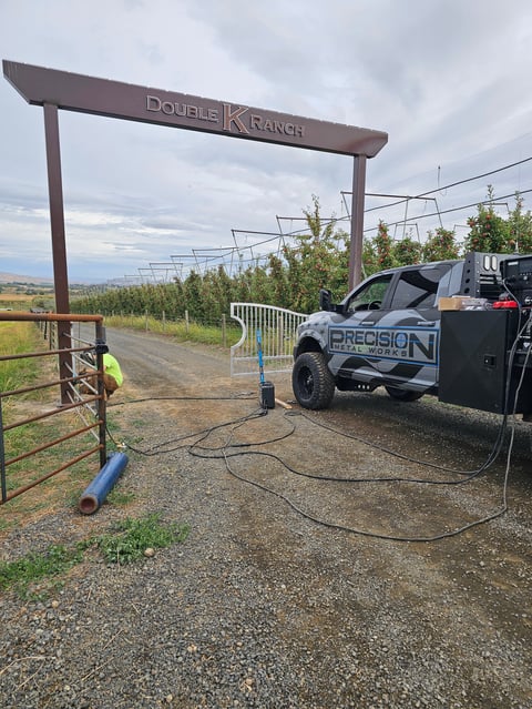 Double K Ranch entrance with work truck parked at gate, rural landscape with orchard trees and rolling hills in background