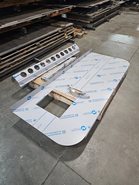 Industrial warehouse floor with white protective panels, metal components, and wooden frames laid out for assembly or manufacturing