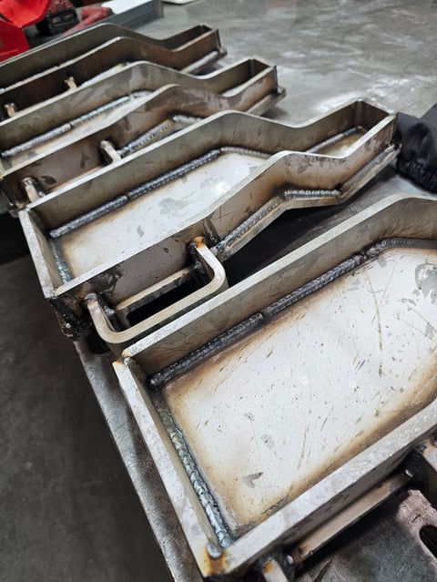 Metal baking trays and sheet pans stacked in rows on a concrete floor in an industrial kitchen setting