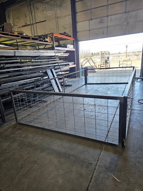 Metal livestock feeding pen with gate panels stacked inside a warehouse with rural landscape visible through windows