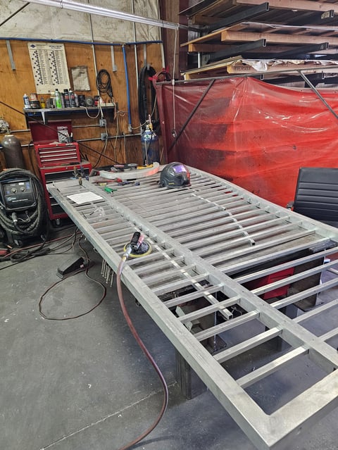 Workshop with boat hull frame under construction, red boat covering, and tools on walls and workbenches