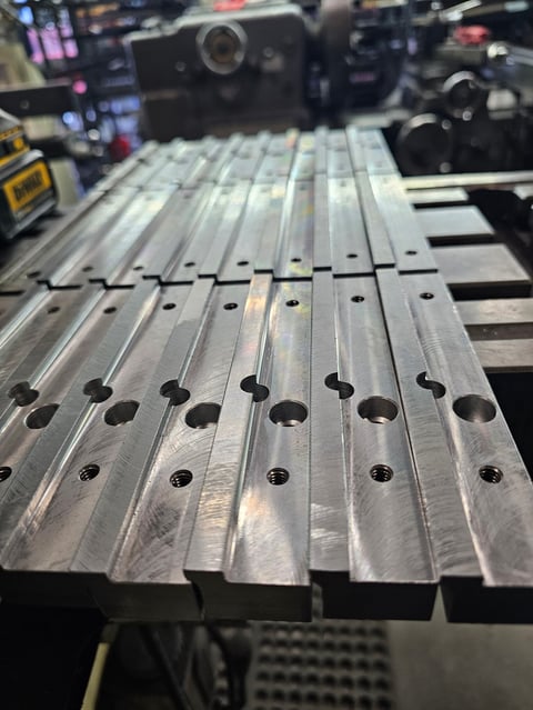 Close-up of metal precision-machined rails with evenly spaced holes in an industrial or manufacturing workshop setting