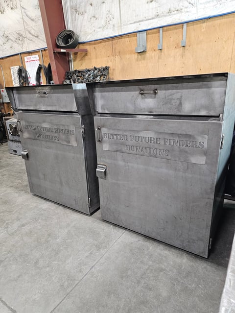 Two large gray metal donation bins labeled Better Future Finders Donations in an industrial warehouse setting