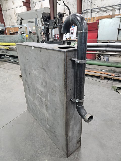 Industrial metal fabrication equipment with curved black ductwork in a workshop setting