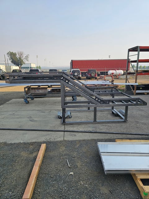 Industrial conveyor belt system with metal frame and rollers in outdoor storage yard with trucks and equipment